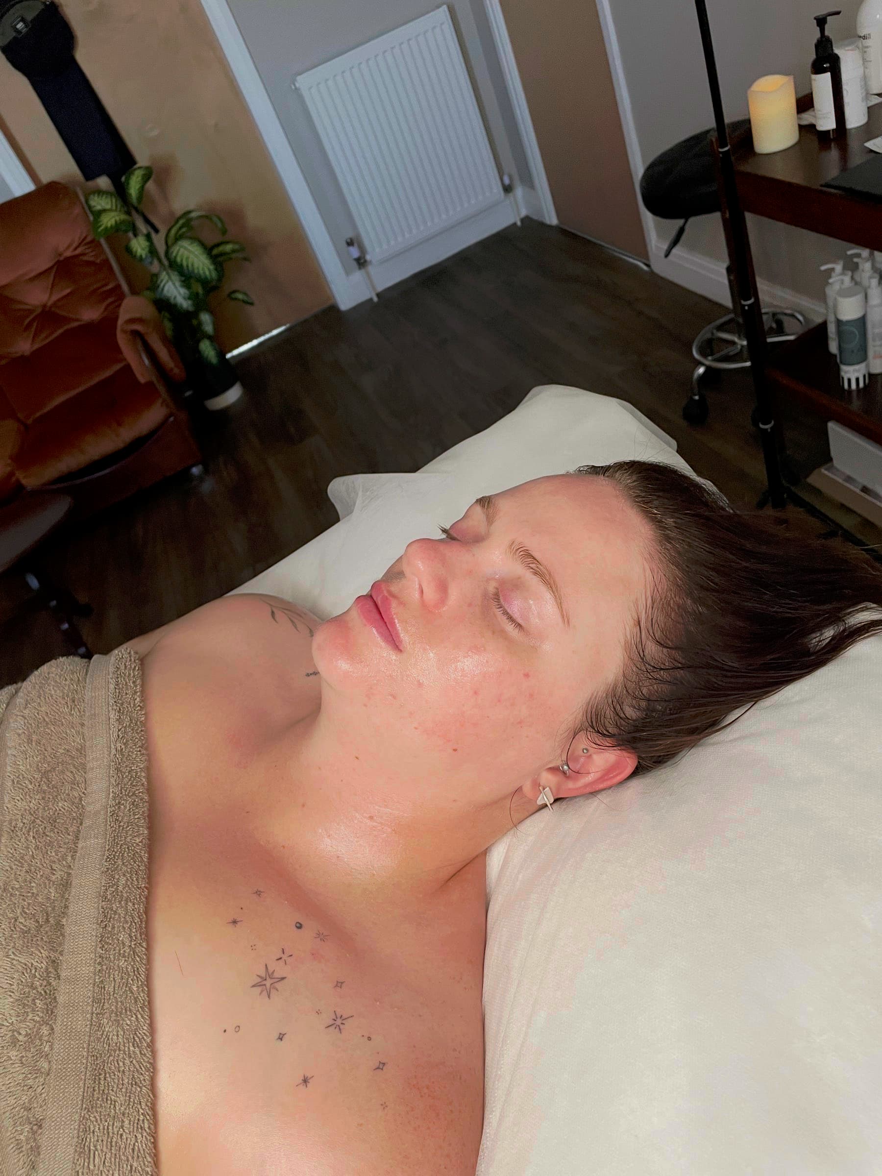 Client lying back on the treatment bed at Fresh Faced after facial lymphatic drainage massage, jawline and neck looking lifted and less puffy.